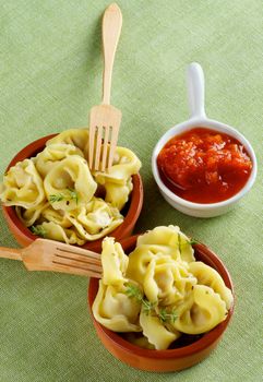 Delicious Meat Cappelletti in Ceramic Bowls with Tomatoes Sauce and Wooden Forks closeup on Green Napkin background