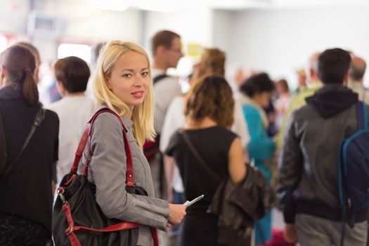 Young blond caucsian woman waiting in line with plain ticket in her hands. Lady standing in a long queue to board a plane.