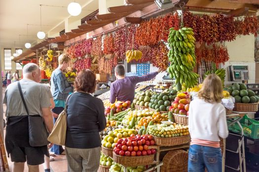 Funchal, Portugal - June 3, 2013: Market in Funchal, Madeira. Booth with merchant trading fruits and spices with tourists.