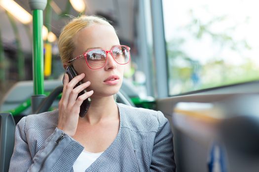 Blonde caucasian business woman talking on cell phone, traveling by bus. Public transport and commuting to work.