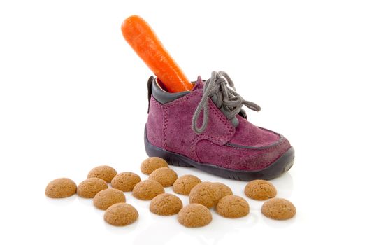 purple little children's shoe with carrot and pepernoten ( ginger nuts), traditional for Sinterklaas in the Netherlands over white background