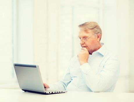 technology, oldness and lifestyle concept - old man in eyeglasses working with laptop computer at home