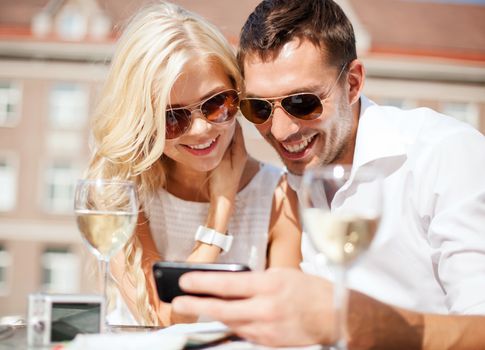 summer holidays, dating and technology concept - couple looking at smartphone in cafe in the city