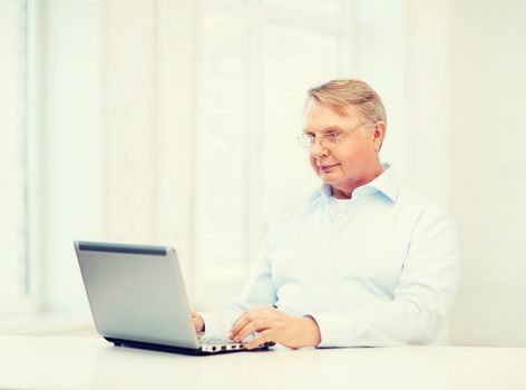 technology, oldness and lifestyle concept - old man in eyeglasses working with laptop computer at home