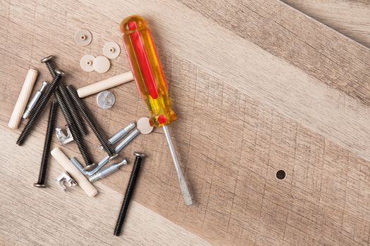 High Angle Still Life View of Yellow Handled Flathead Screwdriver, Screws and Various Pieces of Hardware Beside Small Hole Drilled in Unfinished Planks of Wood