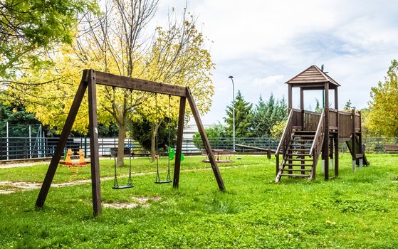 empty swings at playground for child near children stairs slides equipment, on green meadow background