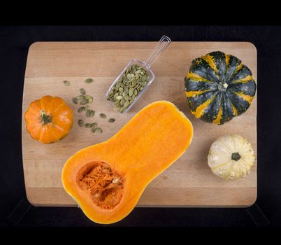 Colorful pumpkins and squash with dried hulled seeds on a wooden table isolated over black