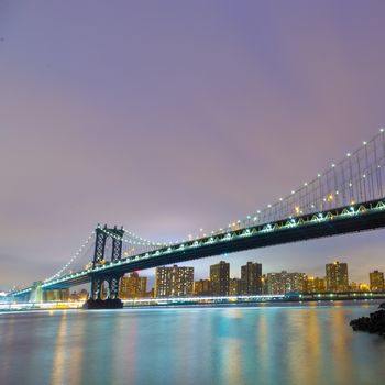 Manhattan bridge and New York City downtown skyline at dusk with skyscrapers illuminated over East River panorama. Square composition. Copy space. 