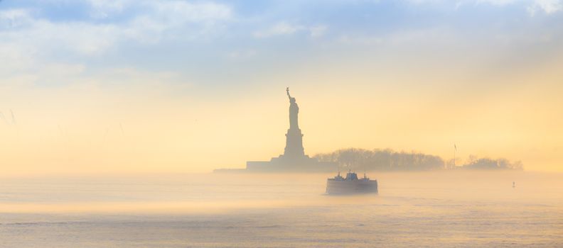 Staten Island Ferry cruises past the Statue of Liberty on a misty sunset. Manhattan, New York City, United States of America. Panoramic composition. Copy space.