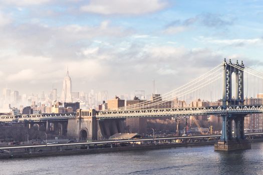 Manhattan bridge and New York City downtown skyline with Chrysler building and skyscrapers illuminated over East River panorama. Horizontal composition.