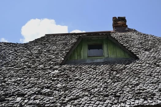 Country house with old roof. The blue sky with white clouds over the house