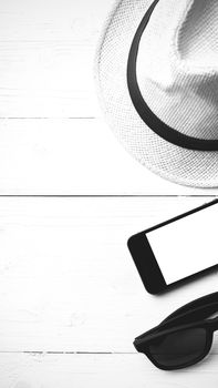 hat sunglasses and smart phone on white table black and white color