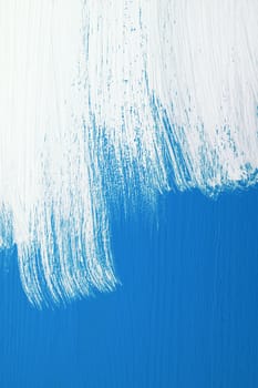 Blue wooden board being roughly painted with a coat of white emulsion paint