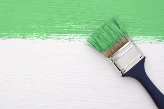 Horizontal stripe of green paint with a dirty paintbrush on a white wooden board