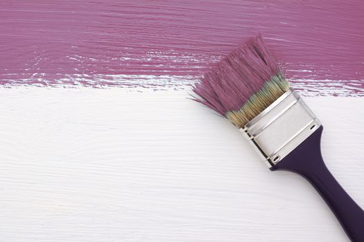 Horizontal stripe of plum-coloured paint with a dirty paintbrush on a white wooden board