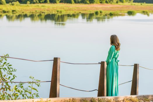 The young beautiful girl walks on an old bridge in the warm autumn weather