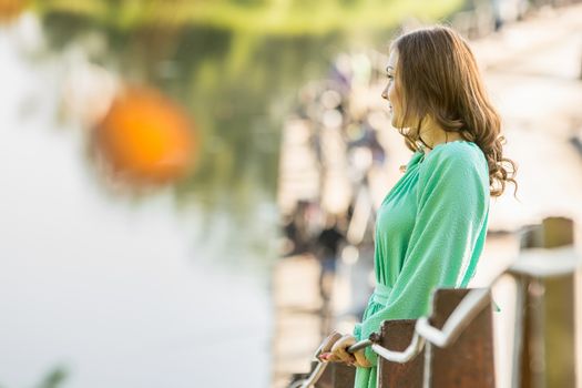 The young beautiful girl walks on an old bridge in the warm autumn weather