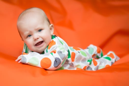Baby girl in a white pjama with big dots lying on a belly on an vibrant orange pillow