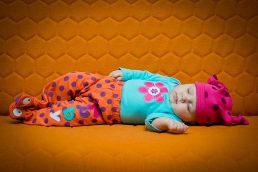 Baby girl sleeping on an orange couch. Bright colors, dots, honey comb
