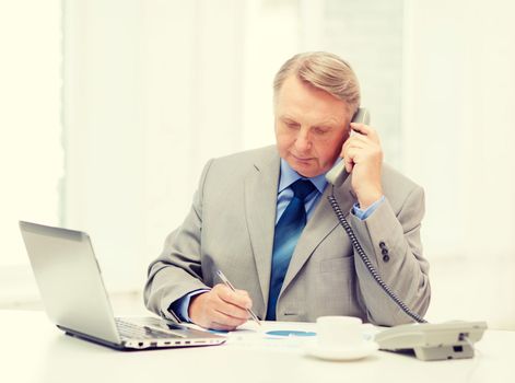 business, technologym communication and office concept - busy older businessman with laptop, charts, coffee and telephone in office