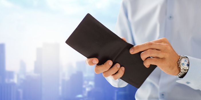 people, business, finances and money concept - close up of businessman hands holding open wallet over city background