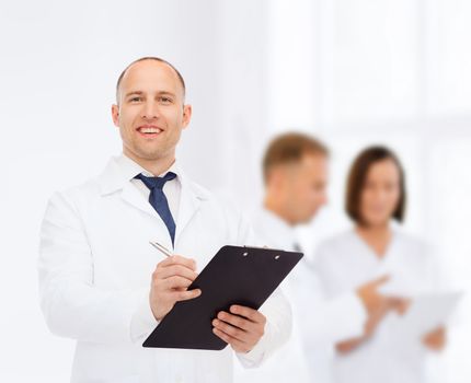 medicine, profession, teamwork and healthcare concept - smiling male doctor with clipboard writing prescription over group of medics