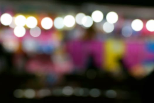 Defocused and blurred image of people at amusement park at night for background usage.