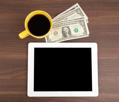 Tablet with coffee and money on wooden table