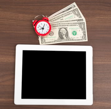 Tablet with money and alarm clock on wooden table