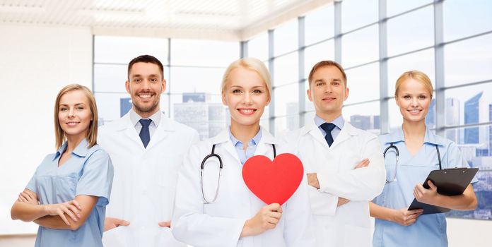 medicine, cardiology, healthcare and people concept - happy young doctors cardiologists with red heart over clinic background