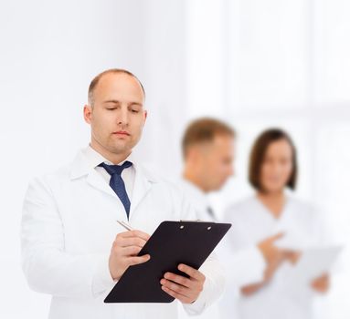 medicine, profession, teamwork and healthcare concept - serious male doctor with clipboard writing prescription over group of medics