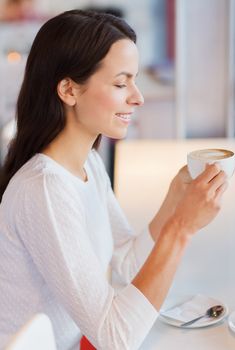 leisure, drinks, people and lifestyle concept - smiling young woman drinking coffee at cafe