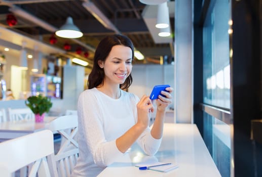 business, people, technology and lifestyle concept - smiling young woman texting message with smartphone at cafe