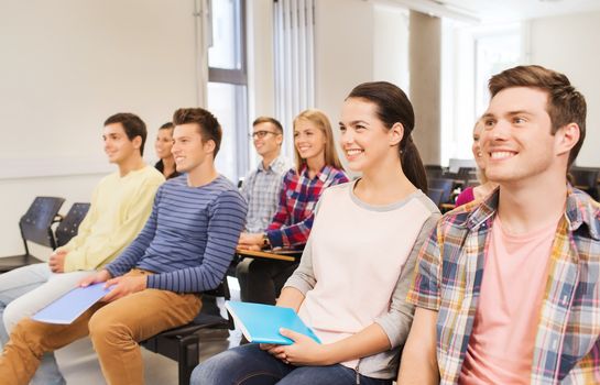 education, high school, teamwork and people concept - group of smiling students with notepads sitting in lecture hall