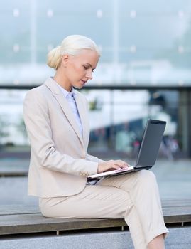 business, education, technology and people concept - businesswoman working with laptop computer on city street