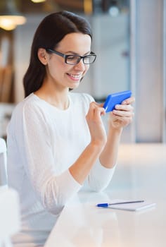 business, people, technology and lifestyle concept - smiling young woman in eyeglasses texting message with smartphone at cafe