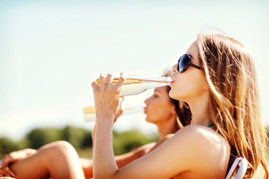 summer holidays and vacation - girls in bikinis with drinks on the beach chairs