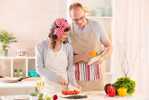 Happy couple reading cookbook and preparing food in the kitchen