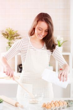 Happy young woman making dough in the kitchen.