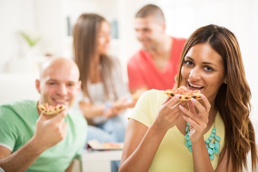 Close up of a young girl smiling and eating pizza with her friends in the background.