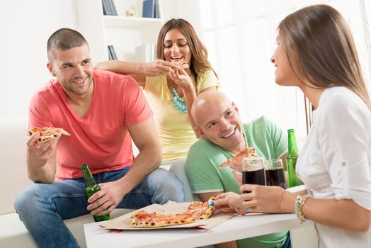 Friends enjoying eating pizza and drink a beer together at home party.