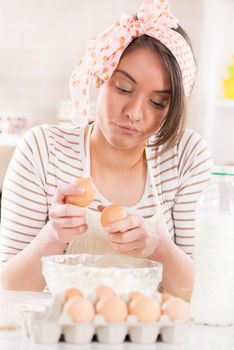 Beautiful young woman making dough in the kitchen. She is breaking eggs.