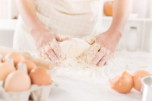 Pair of woman's hands kneading dough on table. Close-up