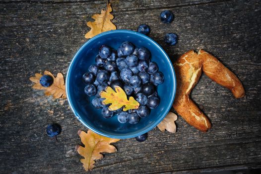 Romantic autumn still life with blackthorn berries in blue bowl and bagel on wooden board