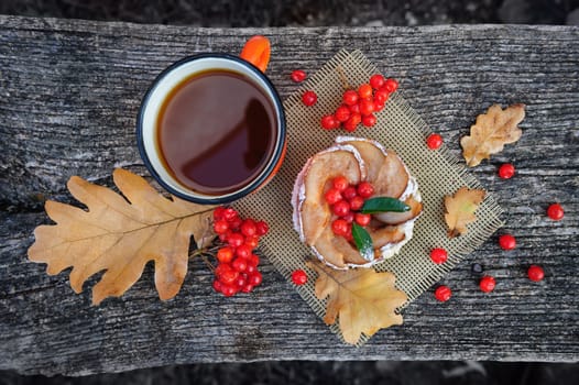 Romantic autumn still life with basket cake, cup of tea, rowan berries and leaves at wooden board, top view