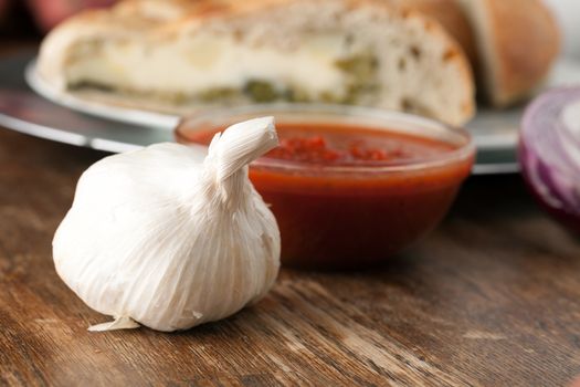 Garlic bulb closeup with tomato sauce and stuffed bread in the background.  Shallow depth of field.