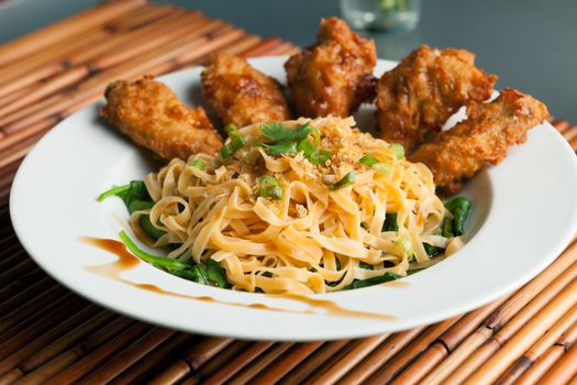 Thai style fried chicken wings on a round white plate with egg noodles and spinach.