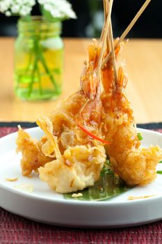 Tempura jumbo shrimp skewers on a white plate standing up vertically.