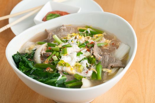 Closeup of some Thai pho style soup with beef and clear rice noodles.