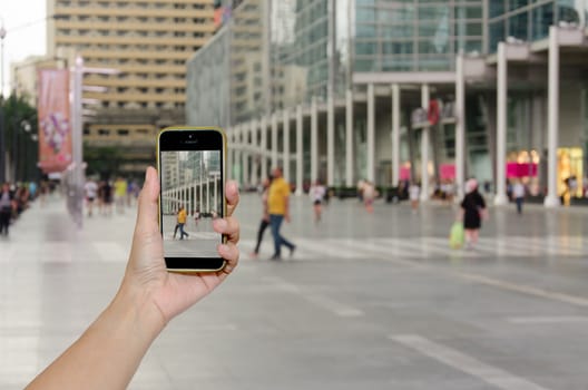 Female hand holding mobile smart phone on people department store outdoor blur background, business concept
